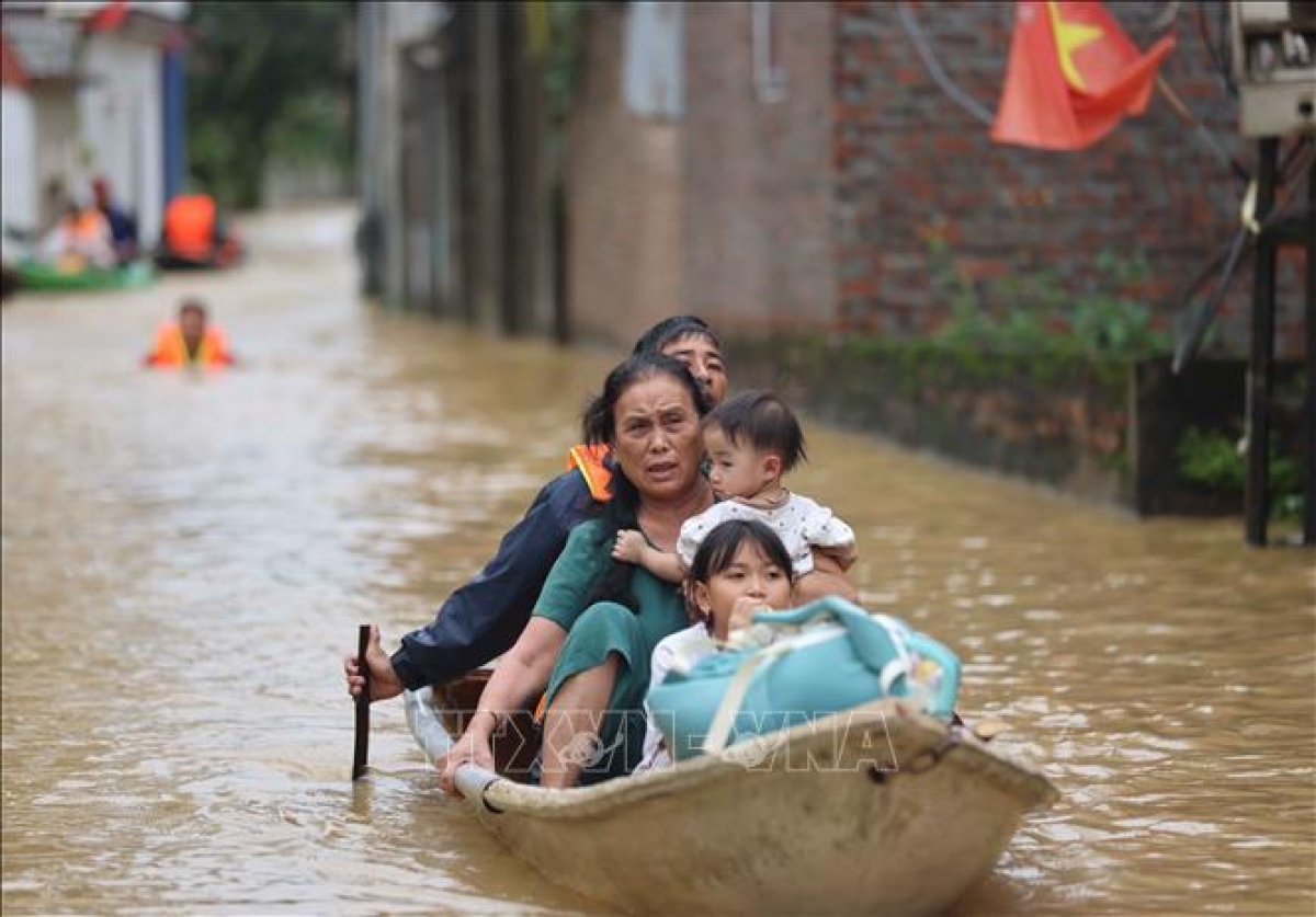 Bà Yến (thôn An Lạc) cùng các cháu được hỗ trợ di chuyển tới nơi an toàn. Ảnh: Thanh Tùng (TTXVN)